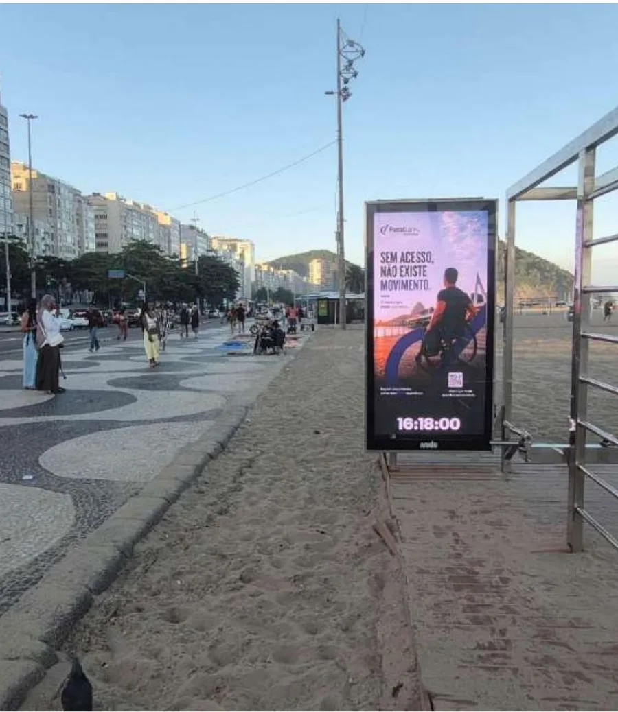Foto real da campanha: painel digital do Parabank na areia da praia de Copacabana, com o Morro do Leme ao fundo